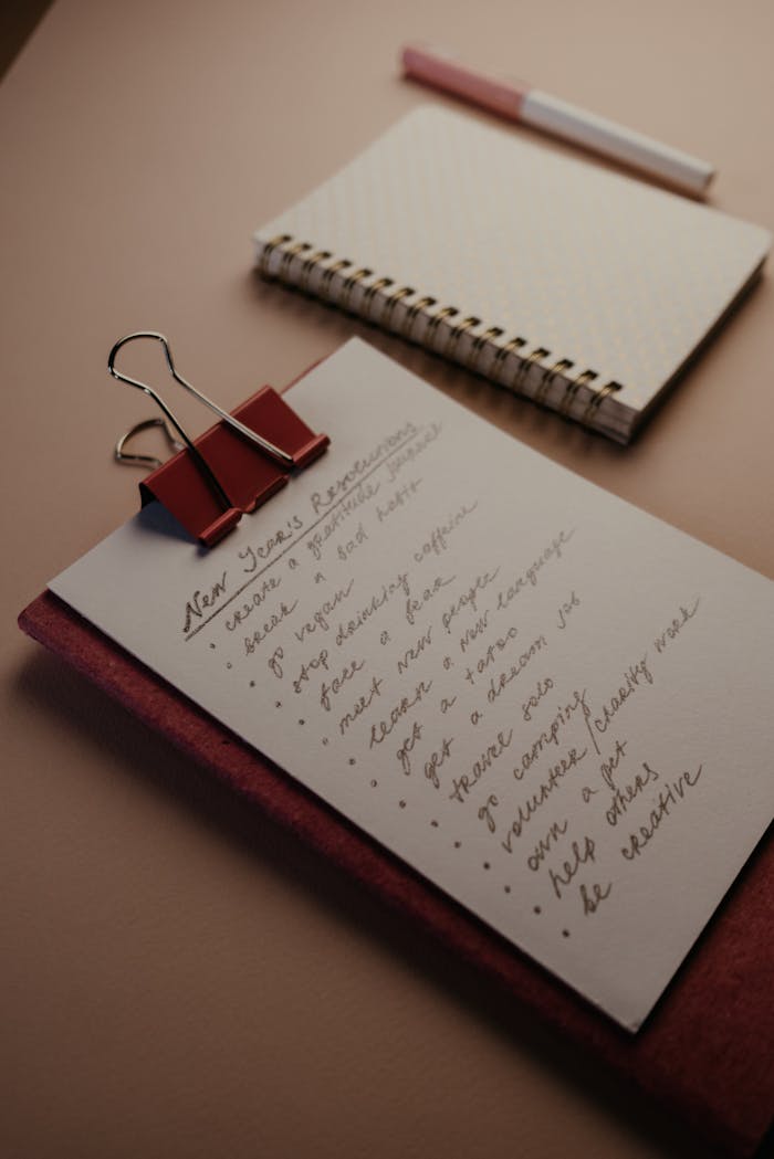 A flat lay of a clipboard with New Year’s resolutions and a notebook on a desk.